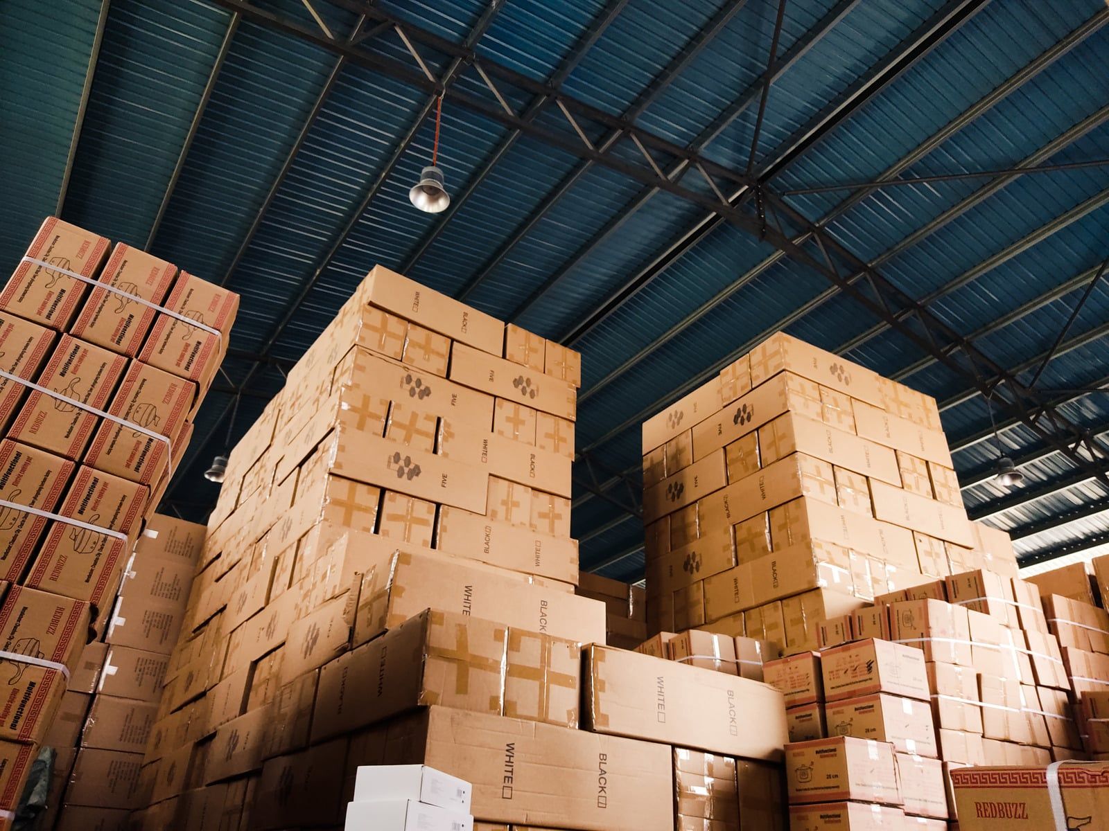 Stacks of cardboard boxes in a warehouse with a blue metal ceiling
