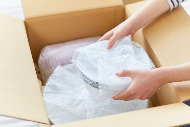 Hands unwrapping a bubble-wrapped item inside a cardboard shipping box