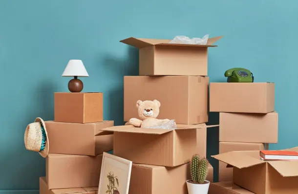 Cardboard boxes stacked into a playful fort with a teddy bear, lamp, cactus, and books against a blue wall