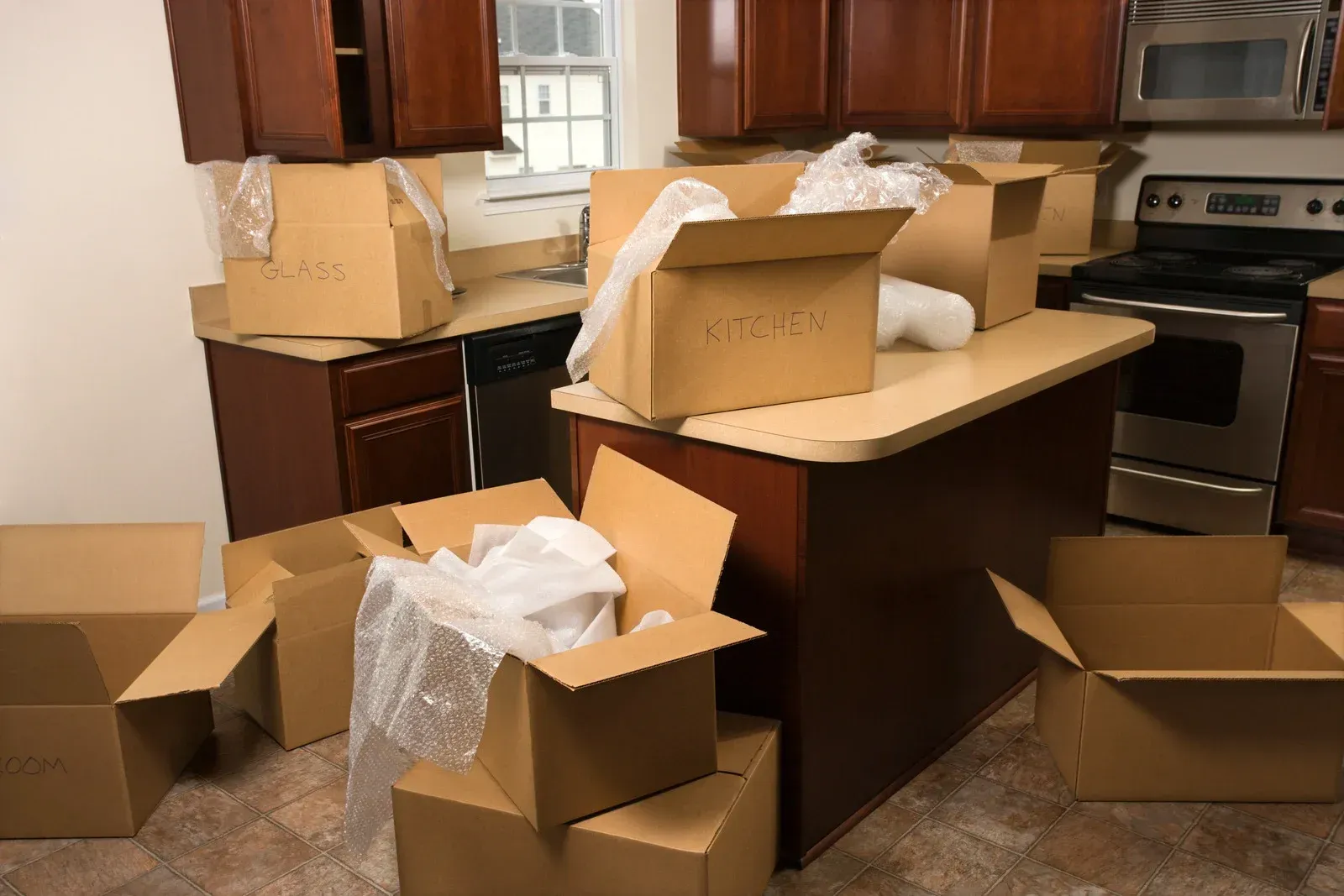 Kitchen with many open cardboard boxes and packing materials on countertops, floor, and island.