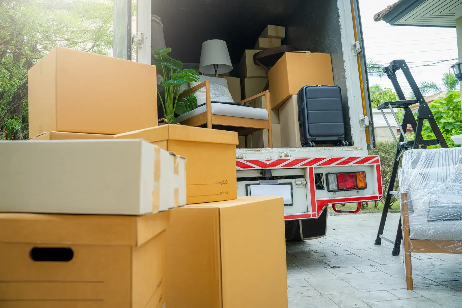 Moving truck loaded with stacked cardboard boxes and furniture at a curbside.