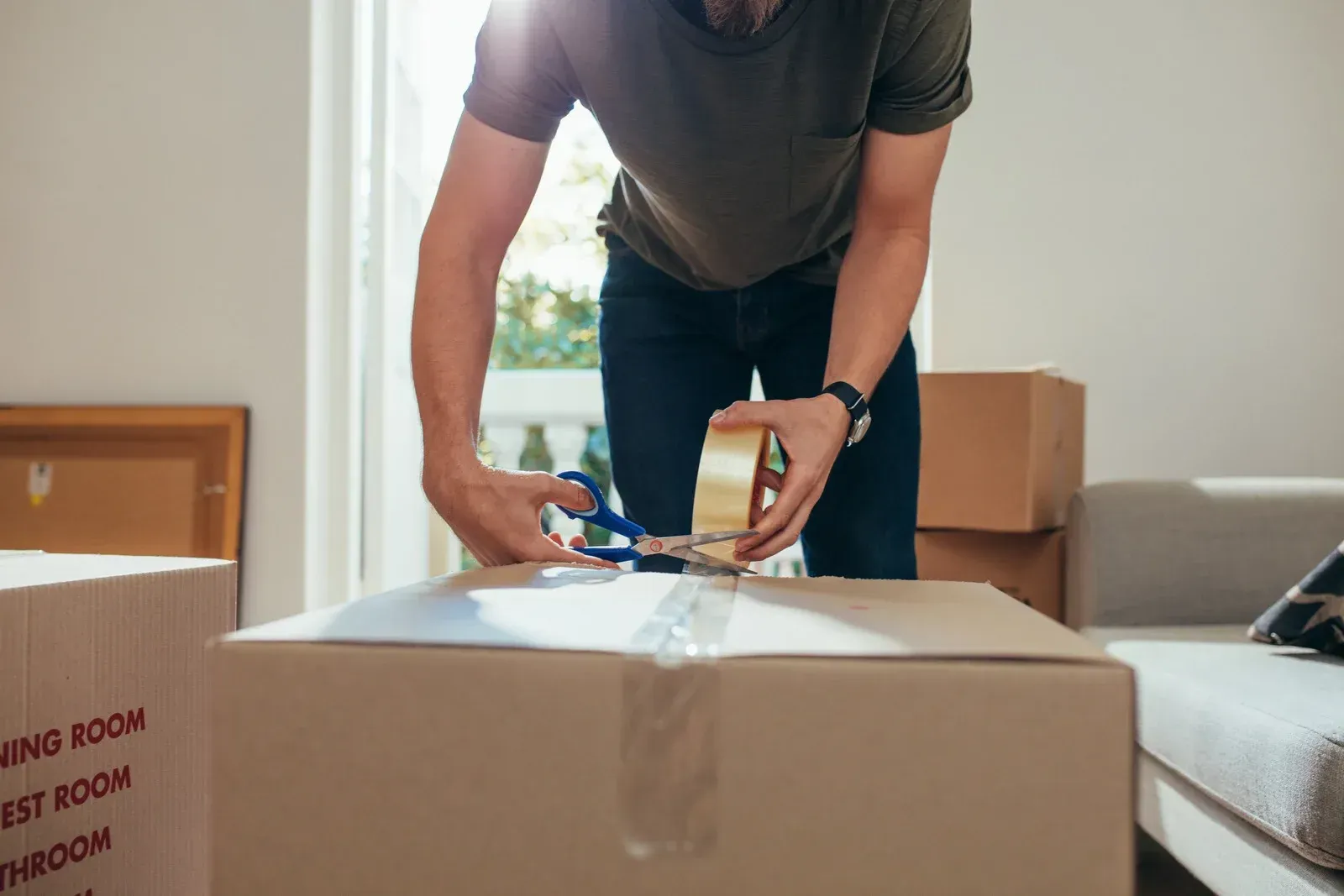 Person taping up a cardboard moving box in a bright room.