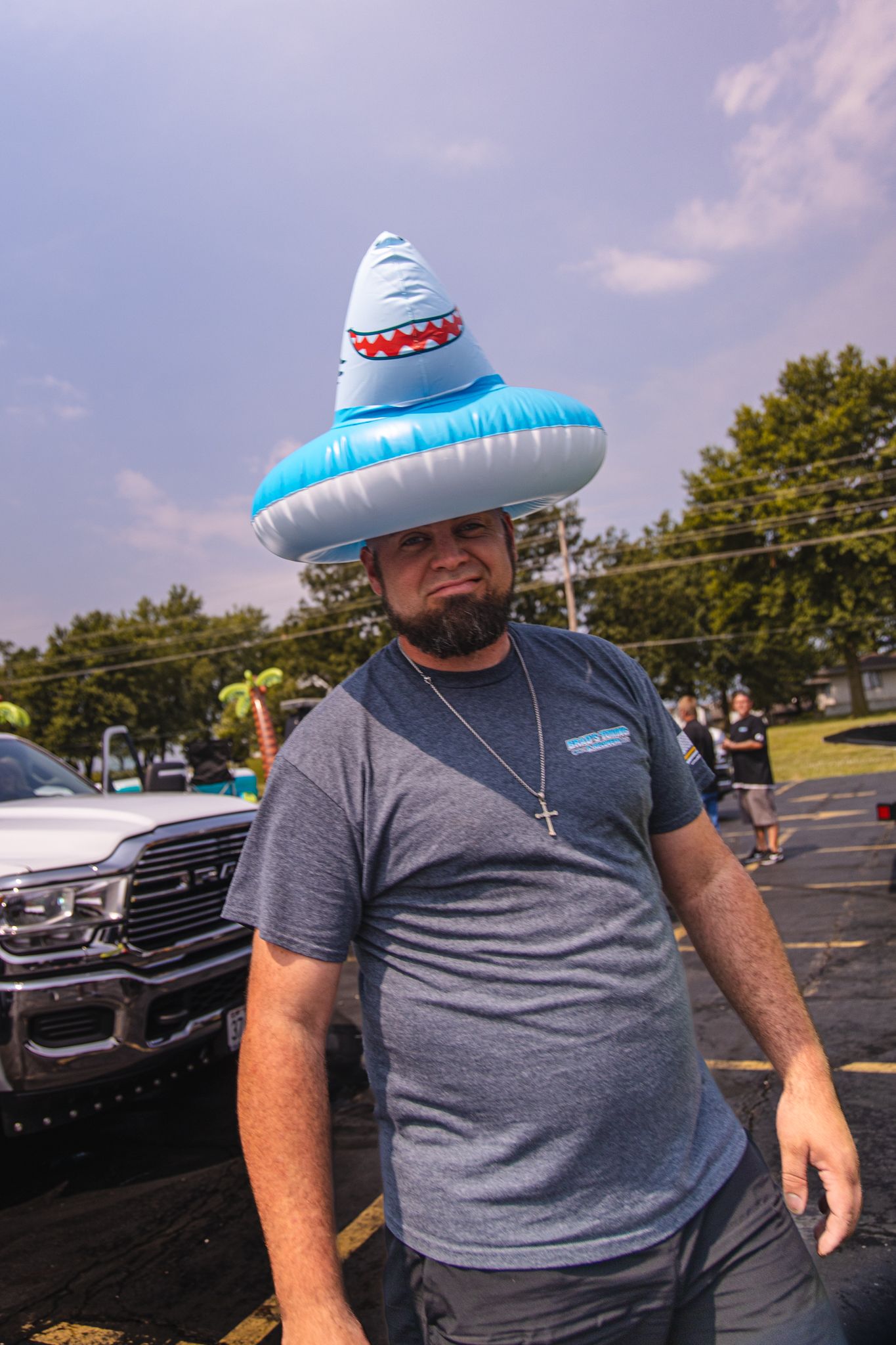 A man is wearing an inflatable shark hat in a parking lot.