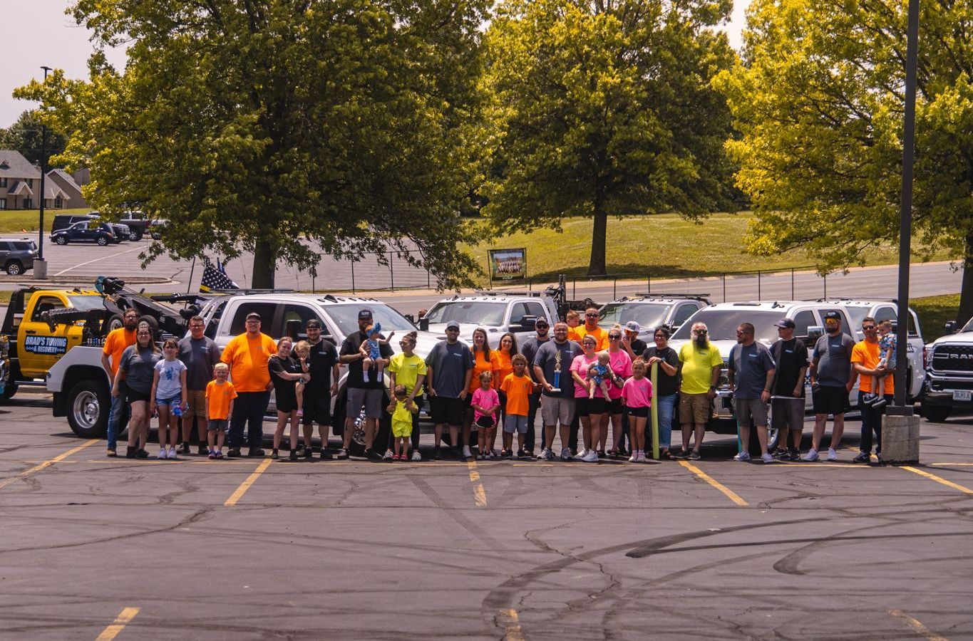 Group of people posing with trucks in a parking lot, some wearing orange, trees in background.