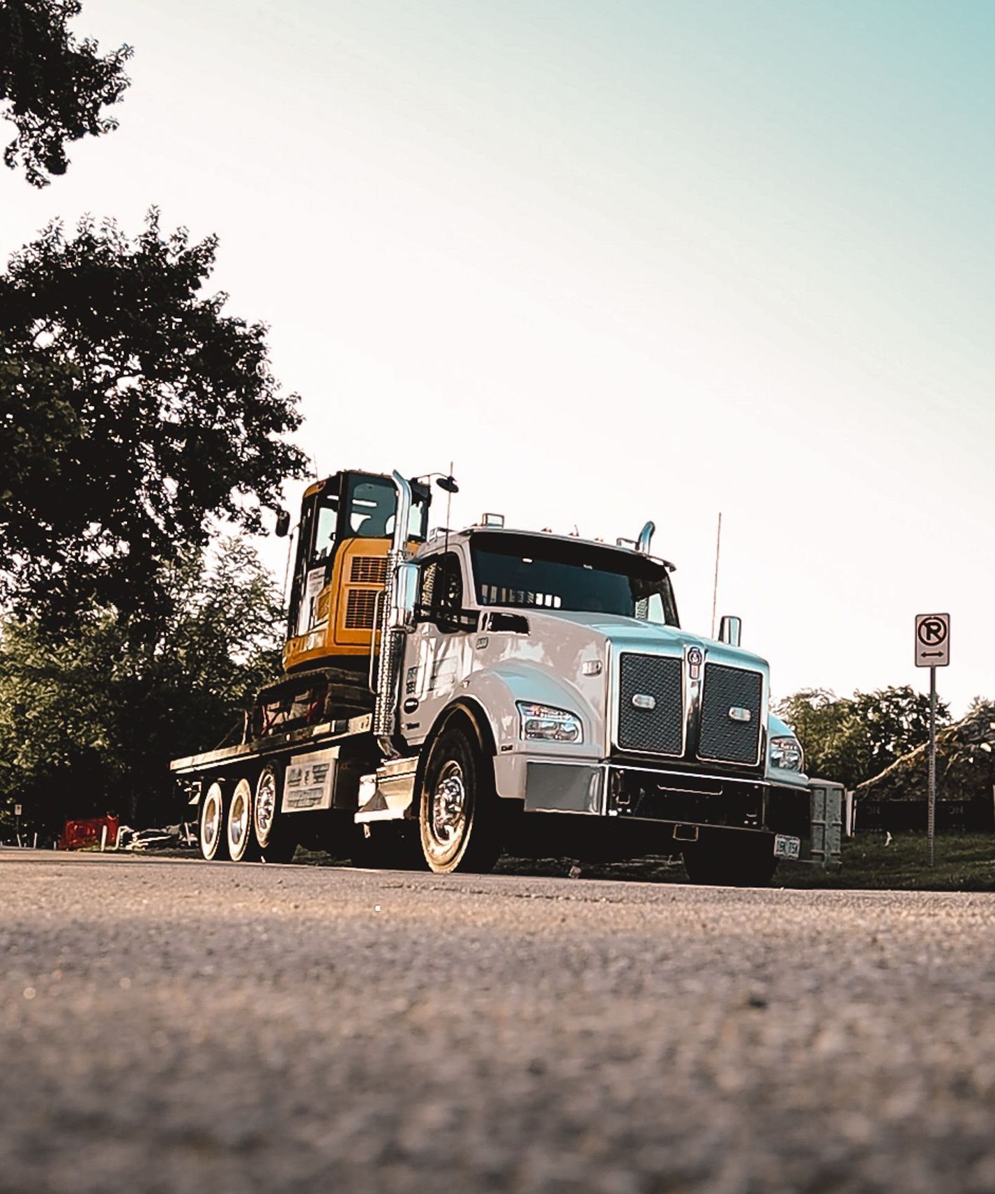 A semi truck is carrying a yellow excavator on the back of it.