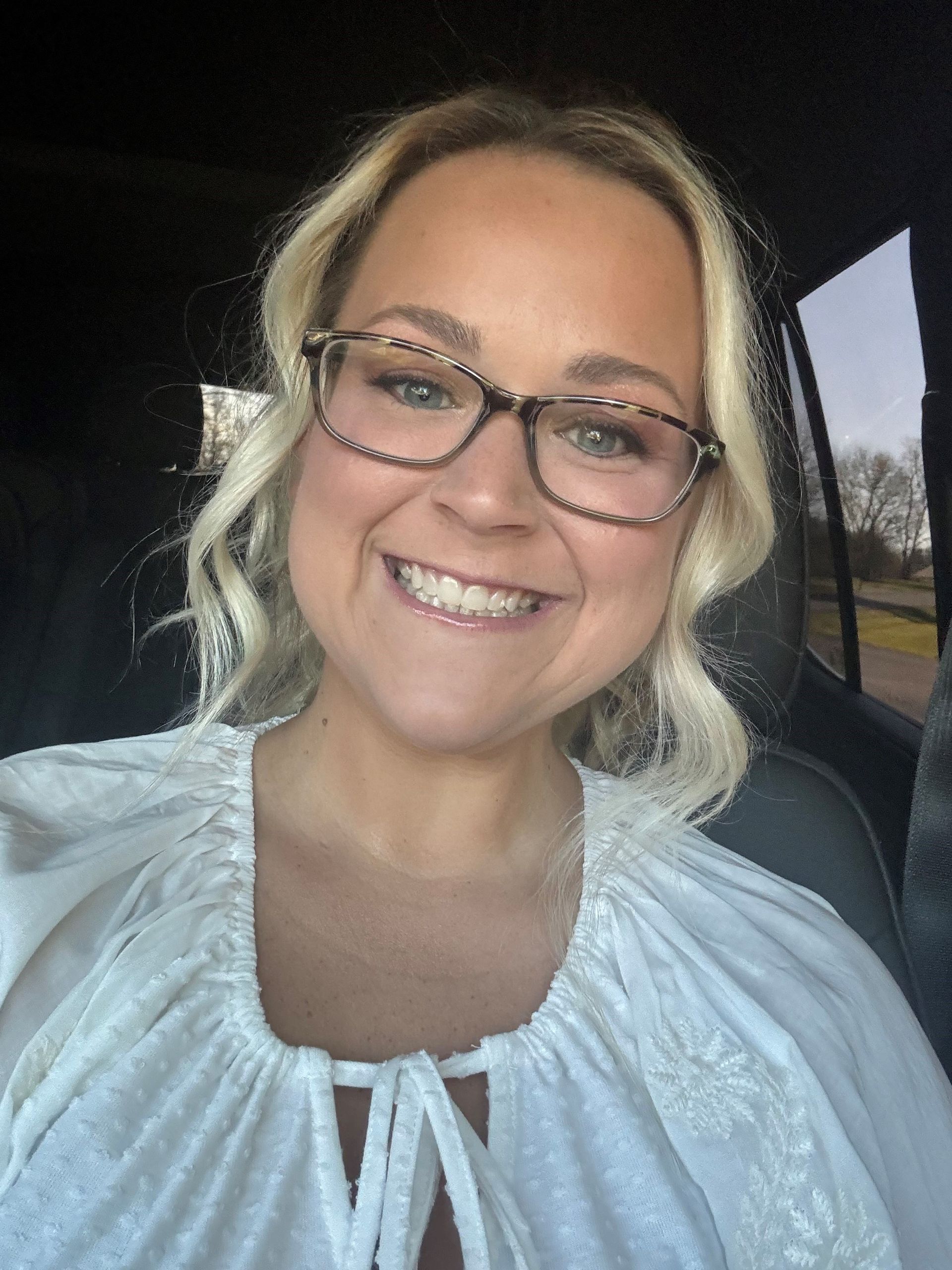 A woman wearing glasses is smiling while sitting in a car.