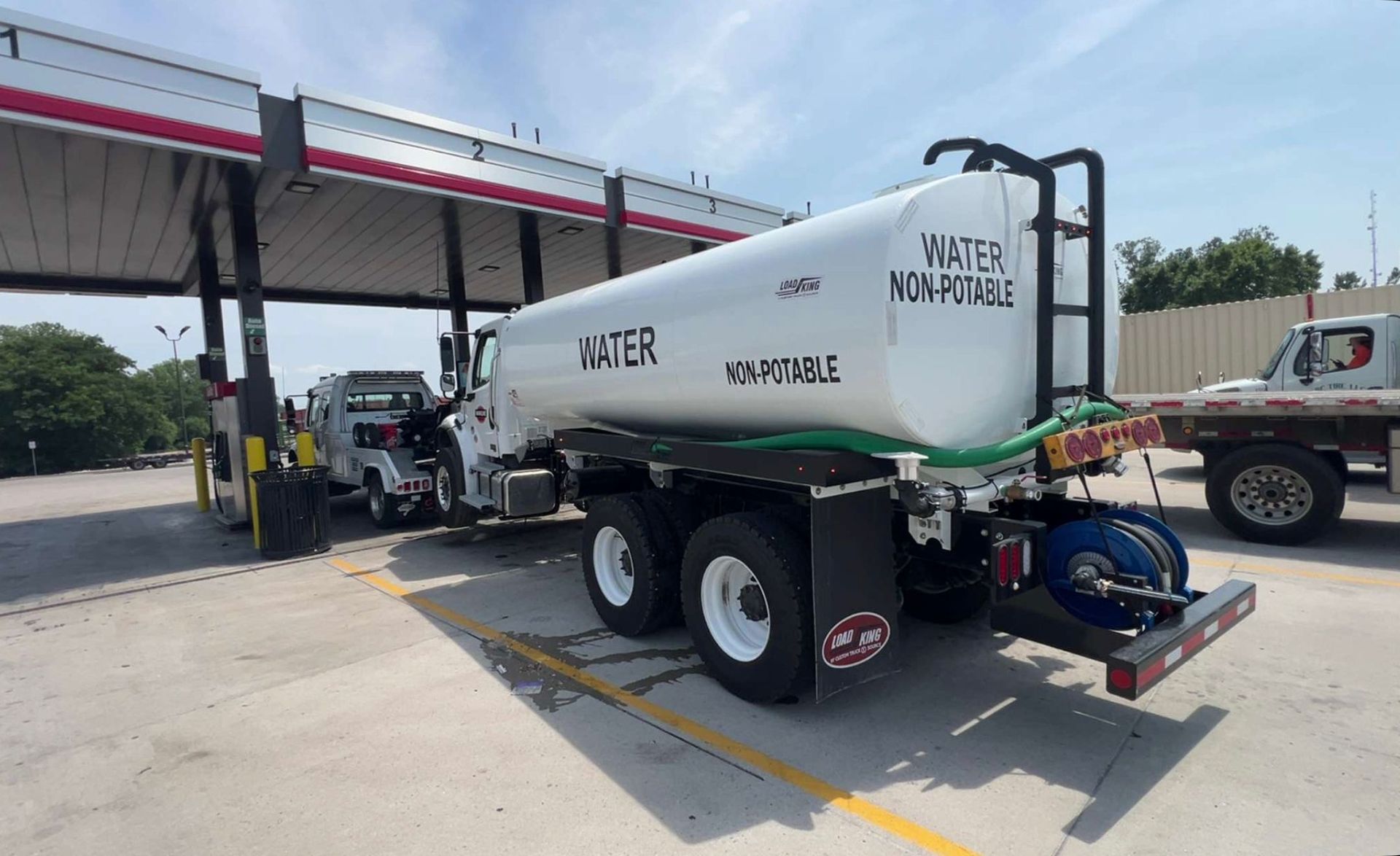 Water tanker truck at a gas pump. White tank labeled