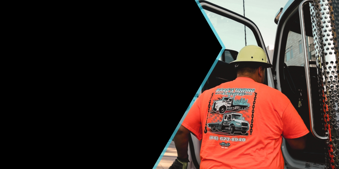 A man wearing a hard hat and an orange shirt is standing in front of a truck.