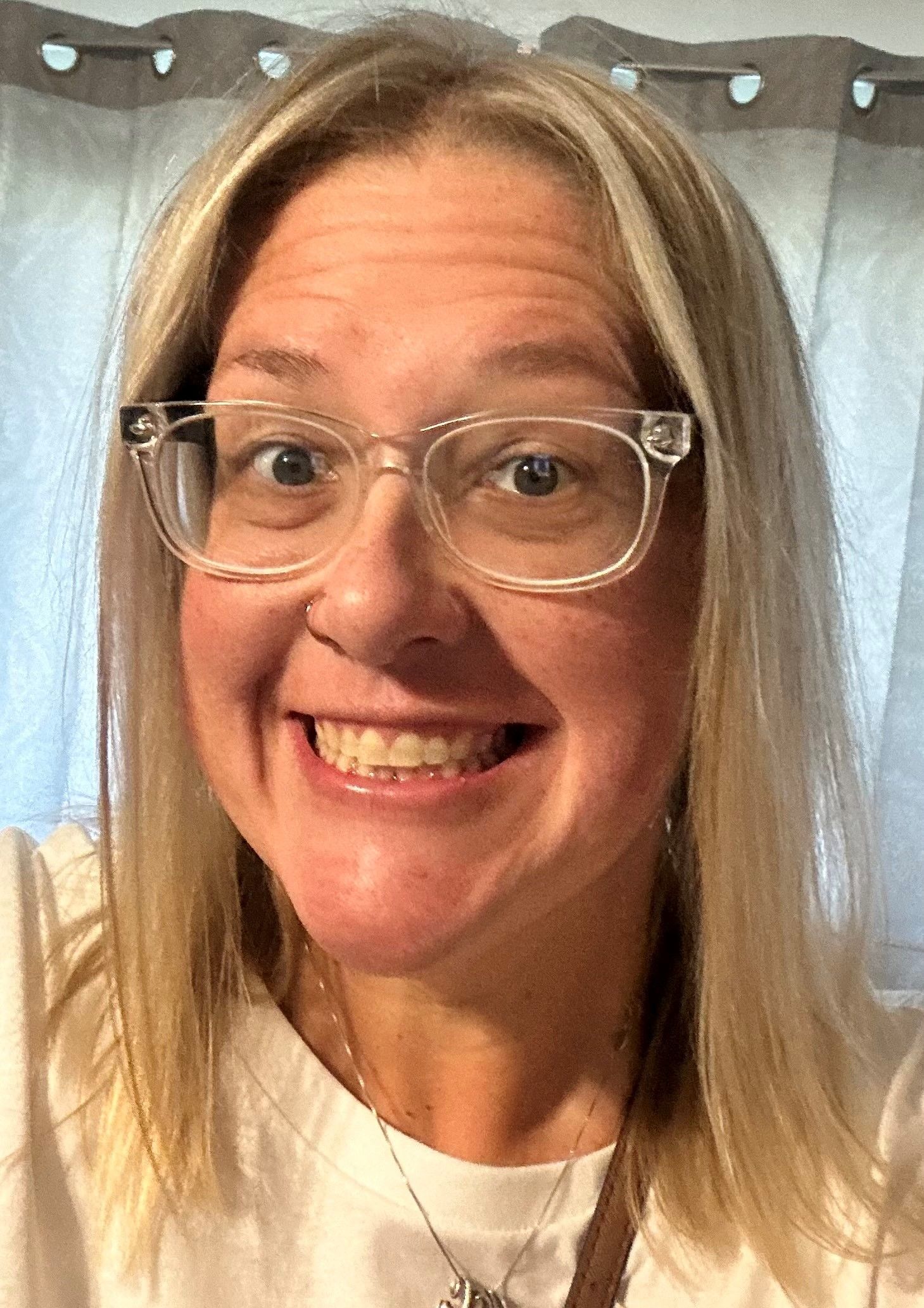 A woman wearing glasses and a white shirt is smiling for the camera.