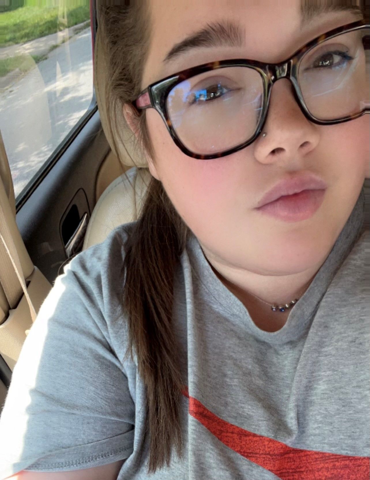 A woman wearing glasses is taking a selfie in a car