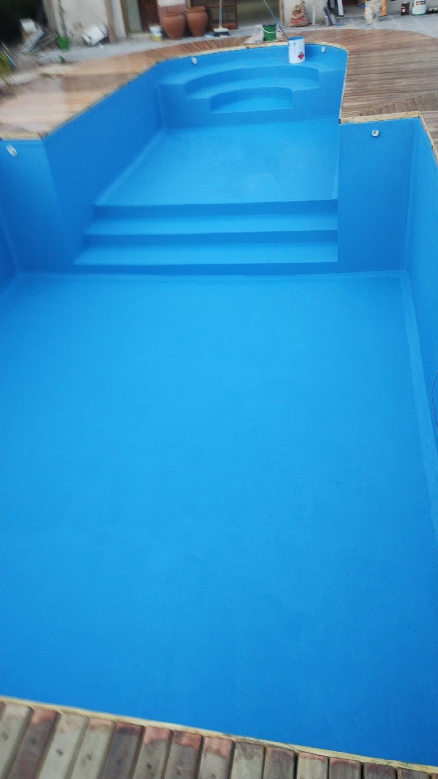 Una piscina azul con escaleras y terraza de madera.