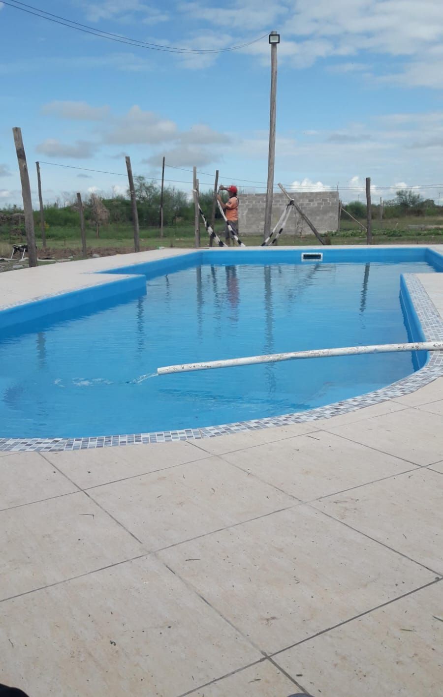 Una gran piscina azul está rodeada por una valla en un día soleado.