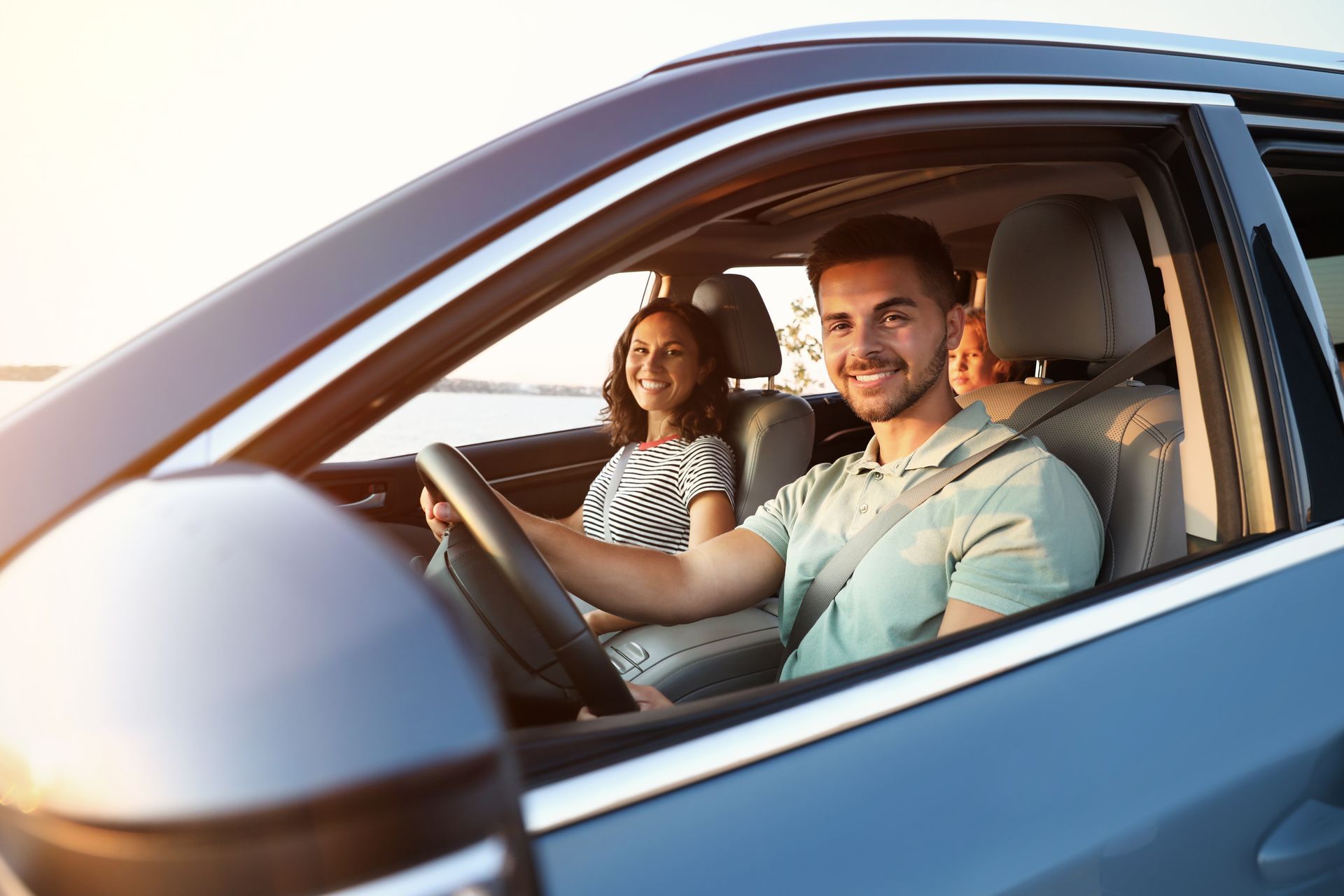 Man driving car, smiling, with woman in passenger seat, sunny day.