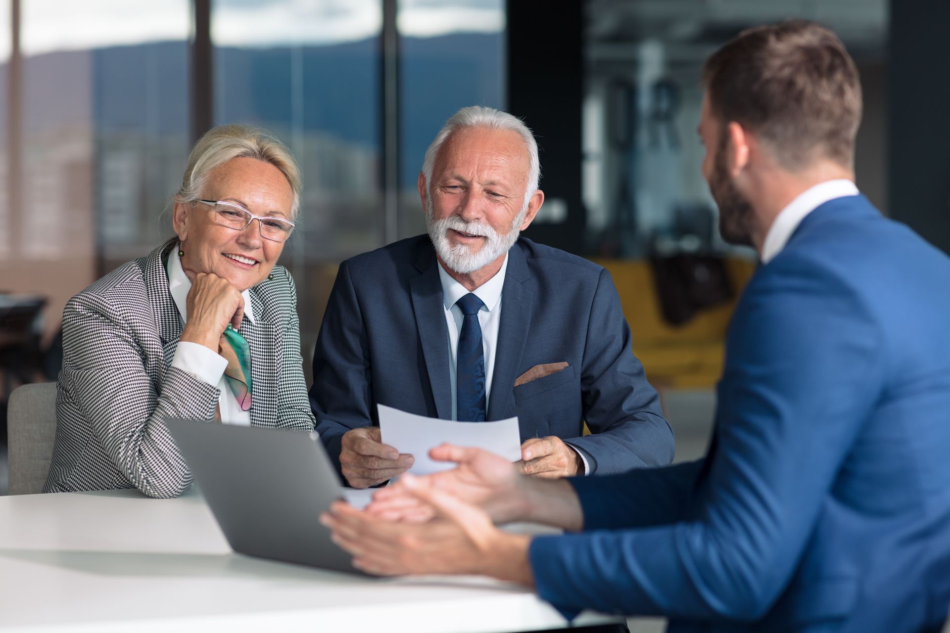 Older couple consulting with a financial advisor at a table; they are looking at papers while the advisor gestures.
