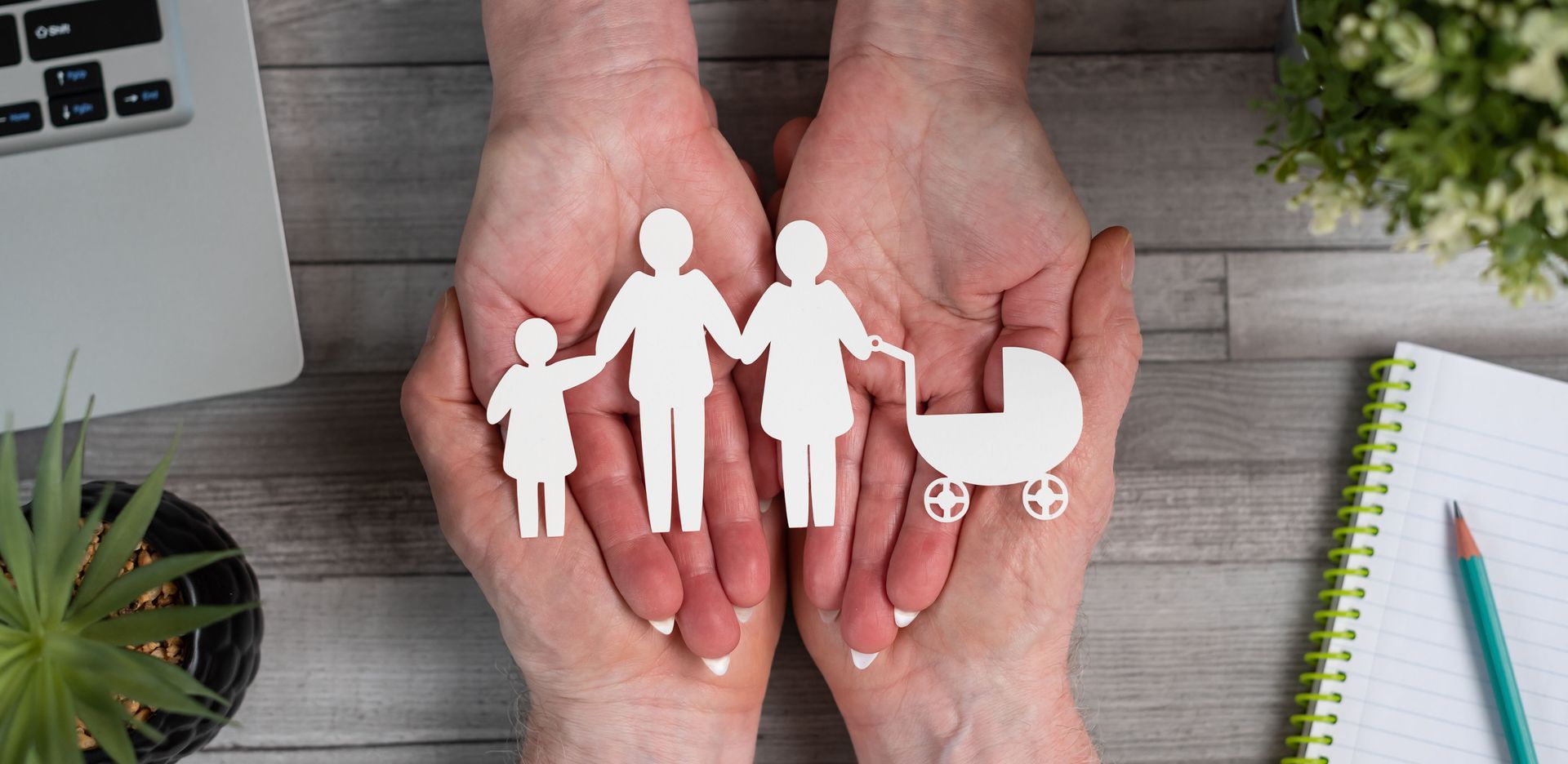 Hands holding paper cutouts of a family: parents, child, baby carriage.