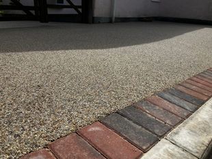 Large resin driveway in a beige colour with red block paviors around the drive.