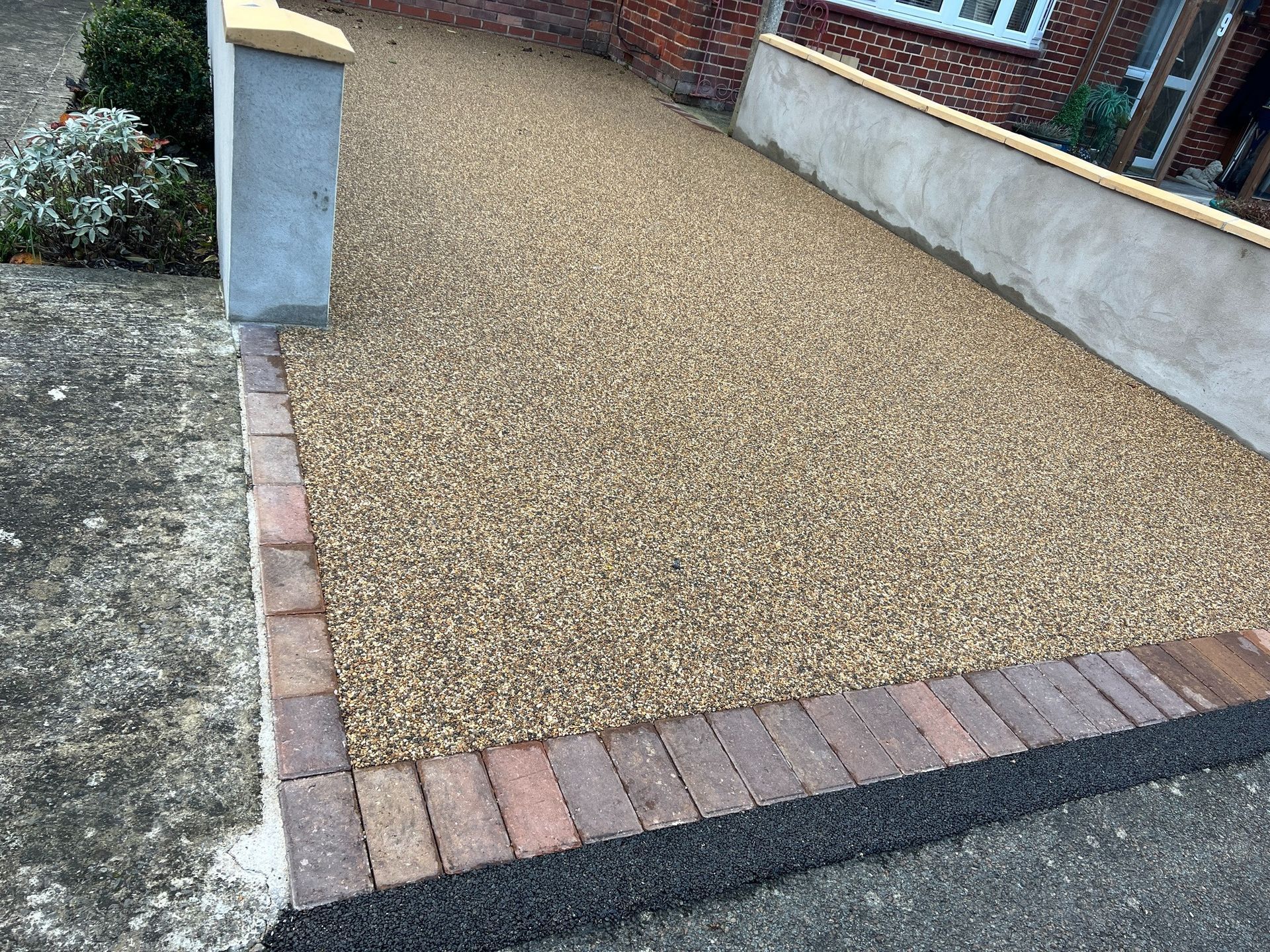 Resin bound driveway completed job in a grey colour with a red-brick bungalow in the background.