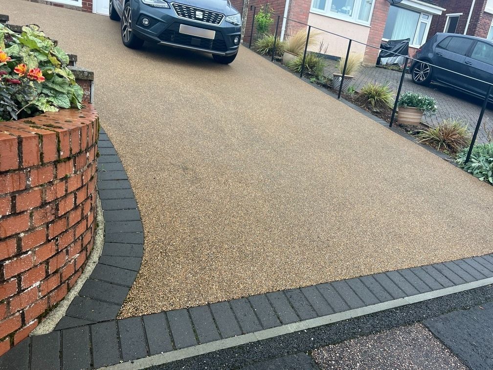 Golden resin driveway with black block paving as the edge.
