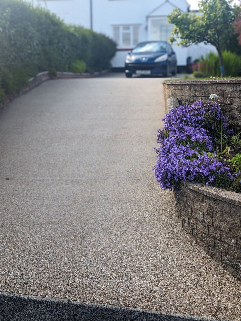 An old resin driveway which is still in really good shape in a golden colour. Flower beds are next to the driveway in the front garden.