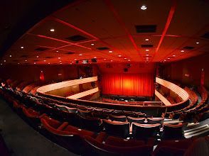 A large auditorium with red seats and a red curtain.