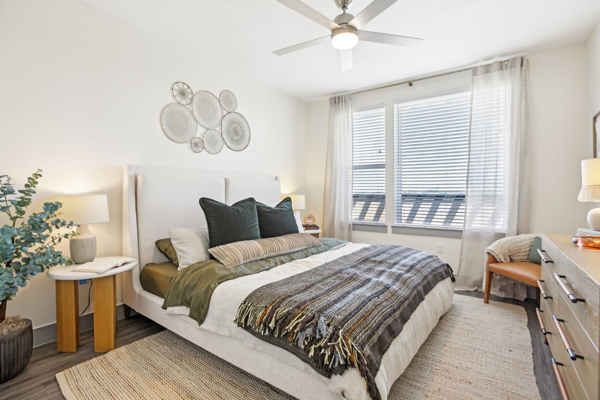 A bedroom with a large bed, ceiling fan, and large windows