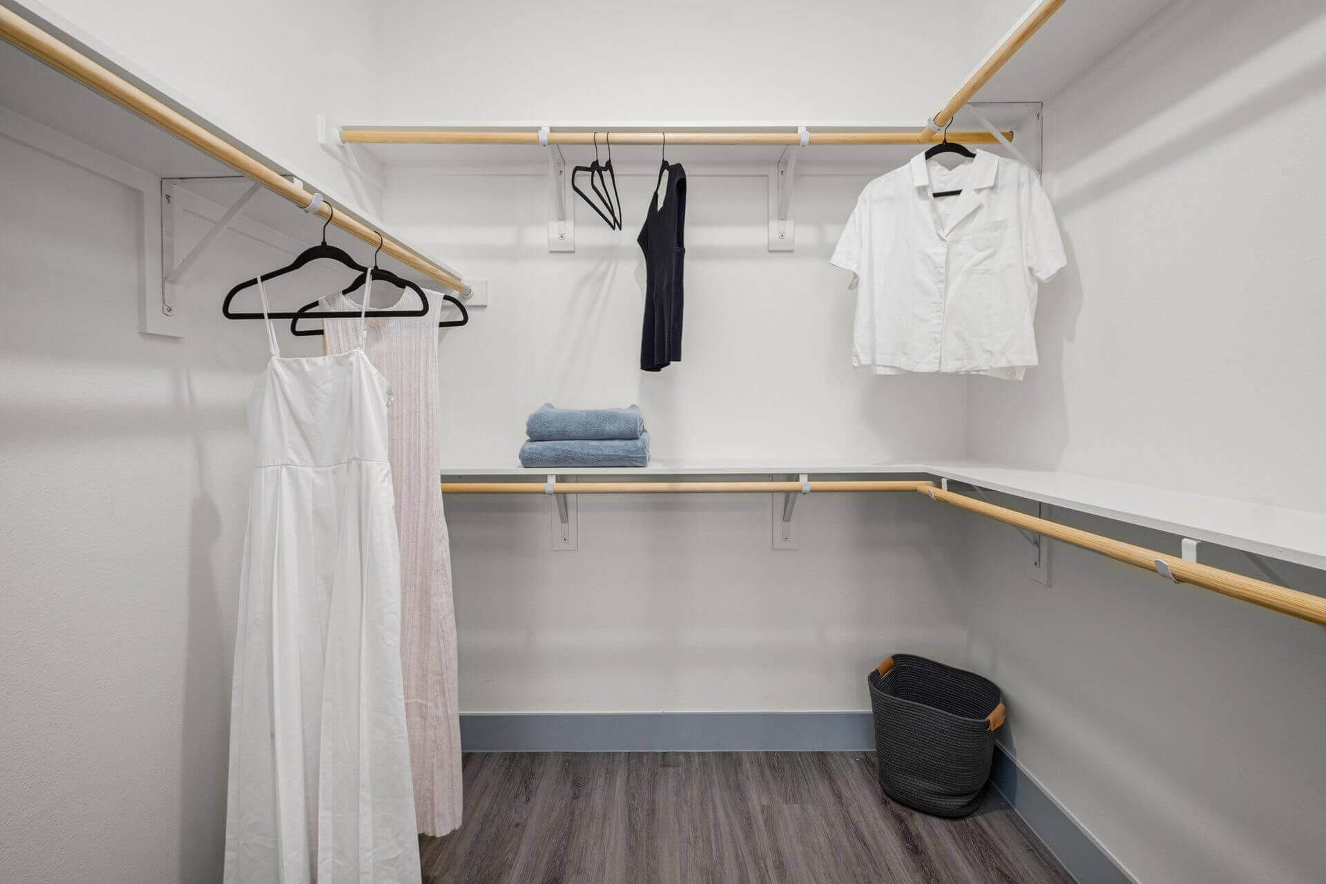 A walk in closet with clothes hanging on racks and a basket.