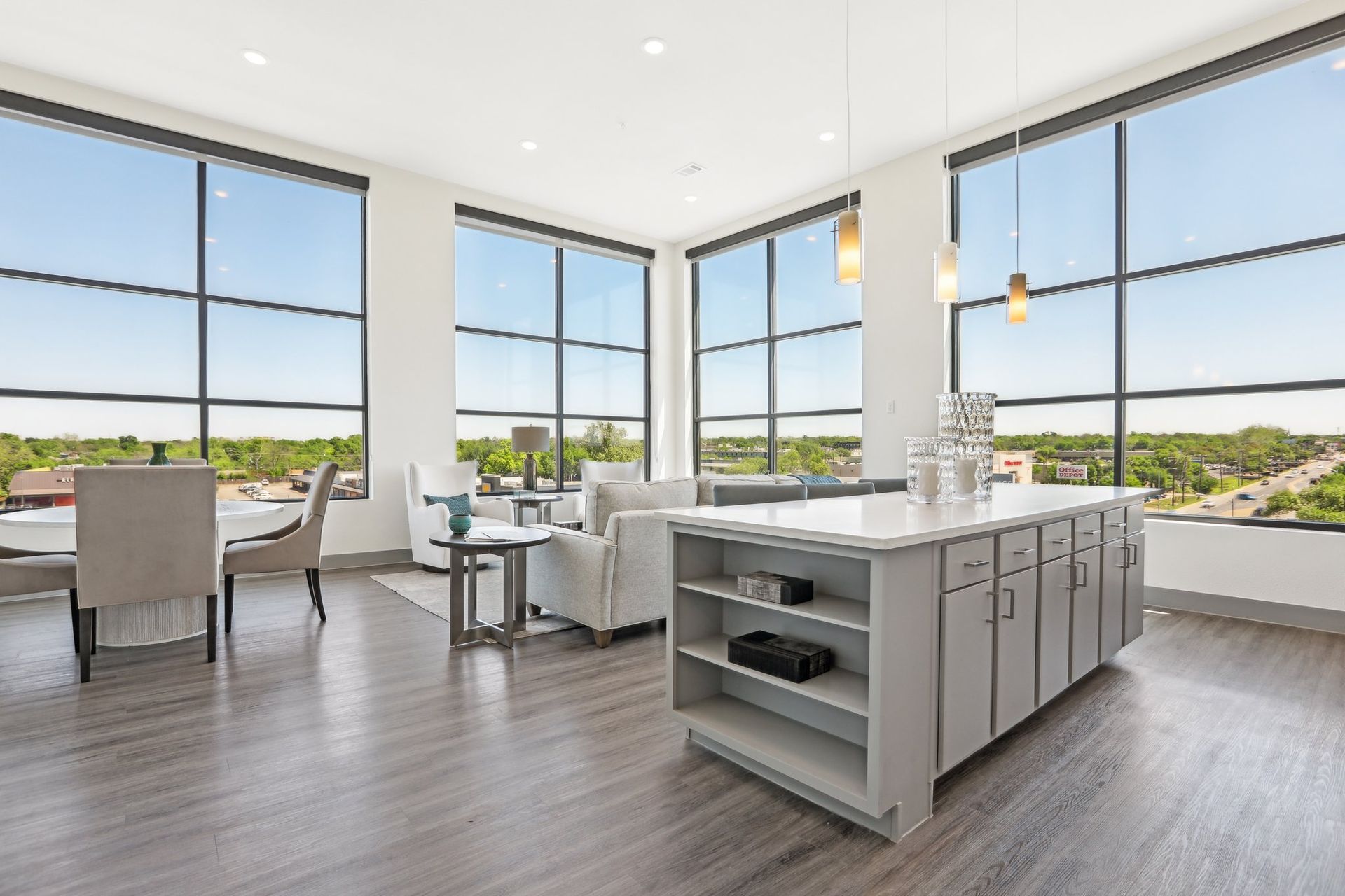 Modern apartment interior with large windows, gray kitchen island, dining area, and living room.