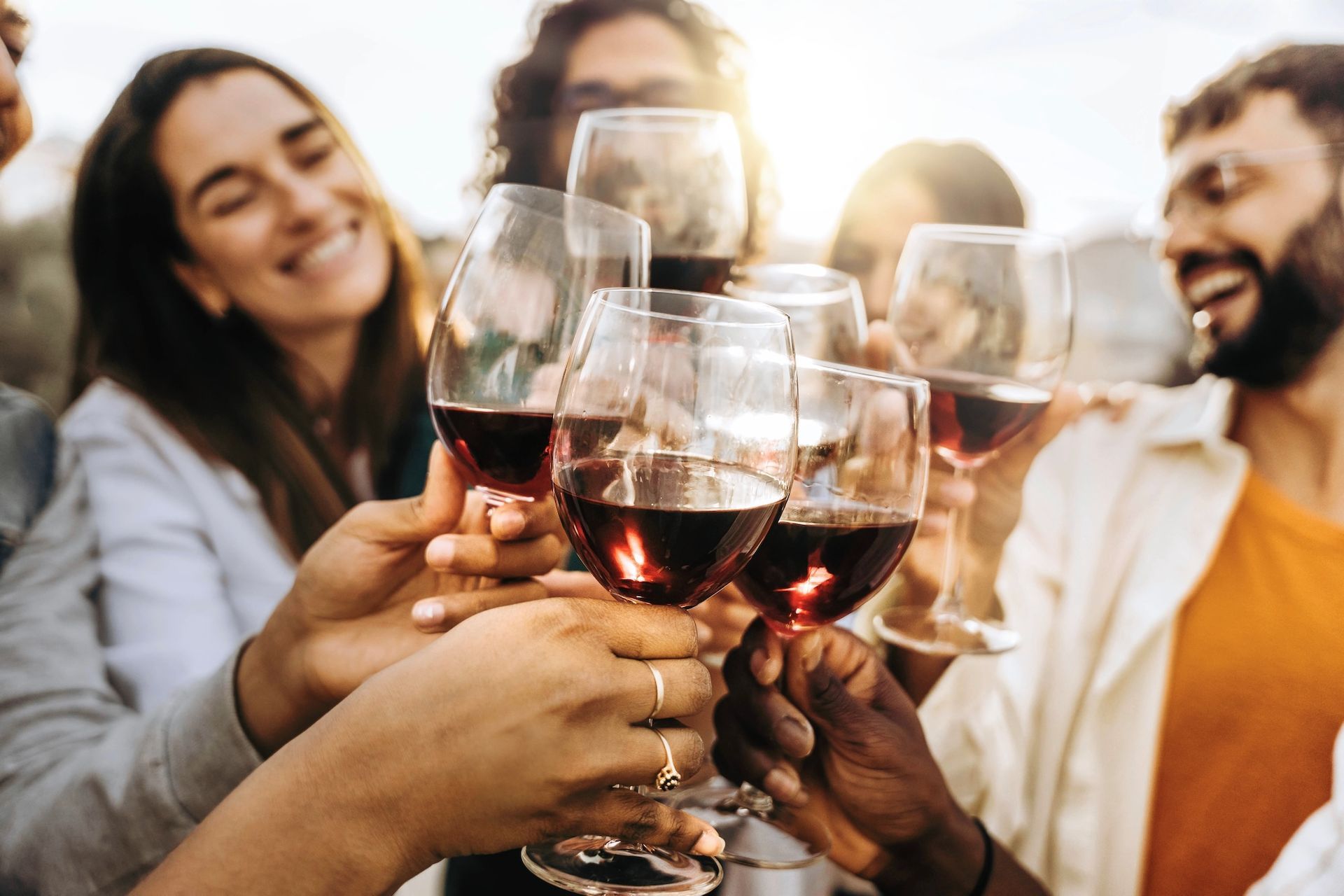 People toasting with red wine glasses outdoors, smiling.