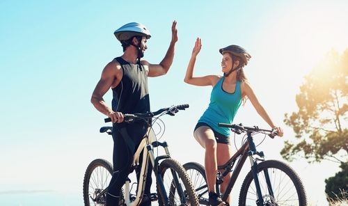 A man and a woman are giving each other a high five while riding bicycles.