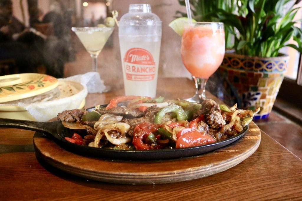 A plate of food and two drinks on a wooden table.