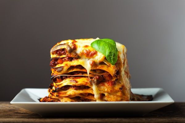 A stack of lasagna on a white plate on a wooden table.