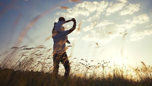 A man is holding a baby on his shoulders in a field.