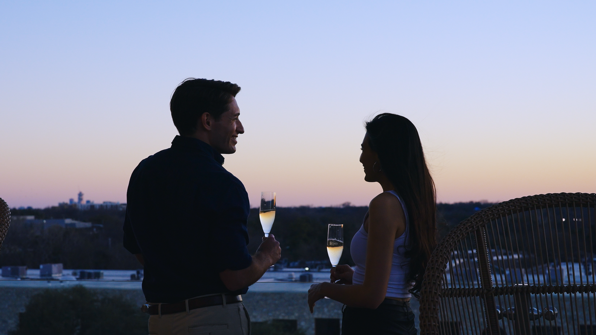 persons toasting champagne on a rooftop at sunset.
