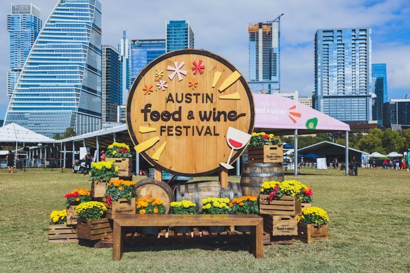 Austin Food & Wine Festival sign with flower boxes, wooden barrels, and downtown Austin skyline in the background.