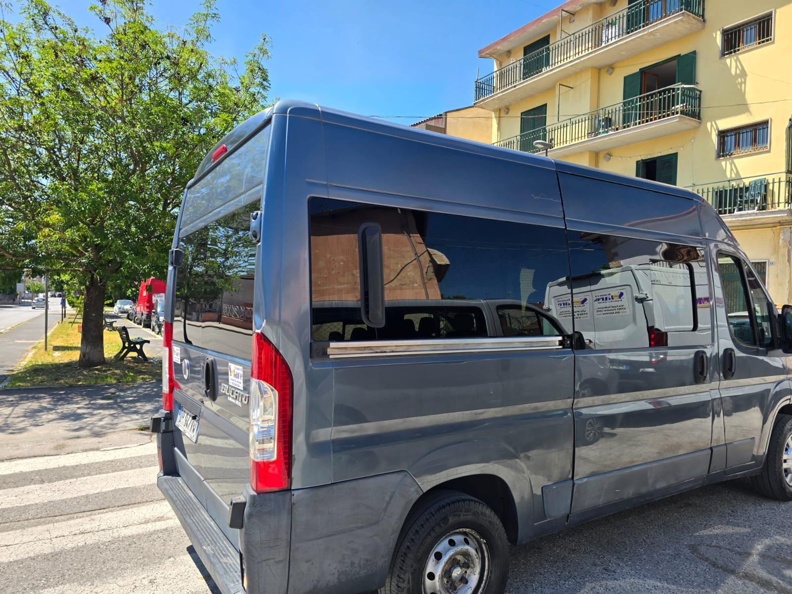 Un fattorino carica scatole di cartone su un furgone argentato con la porta posteriore aperta.