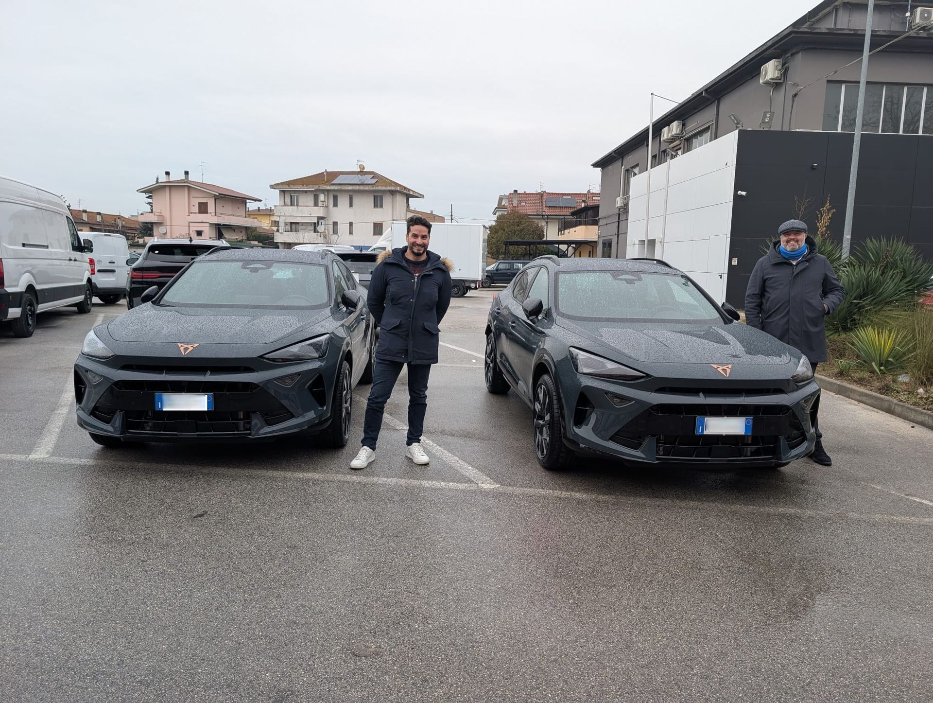 Uomo che aiuta una donna in auto; donna sorridente al volante. Auto scura con interni neri.