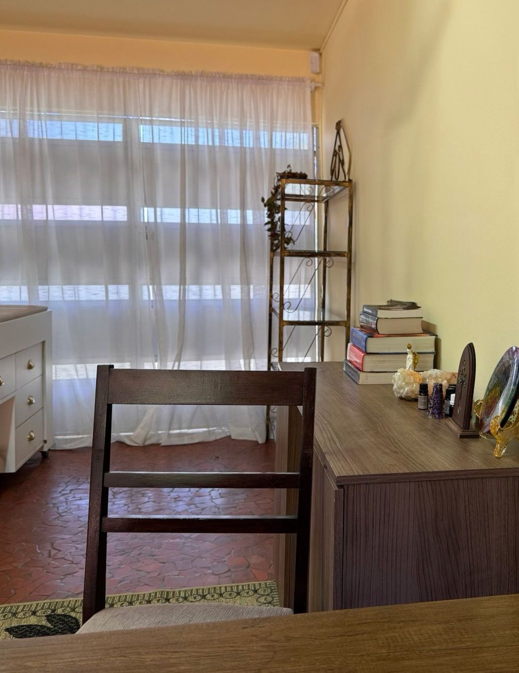 Uma sala com uma escrivaninha, uma maca e uma cadeira em frente a uma janela