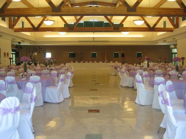 Banquet hall with rows of white chair covers and purple sashes under wooden beams