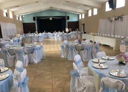 Decorated banquet hall with round tables, white chair covers, and light blue sashes set for an event