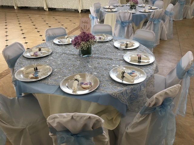 Round banquet table with silver tablecloth, blue chair sashes, and purple flower centerpiece in a decorated hall