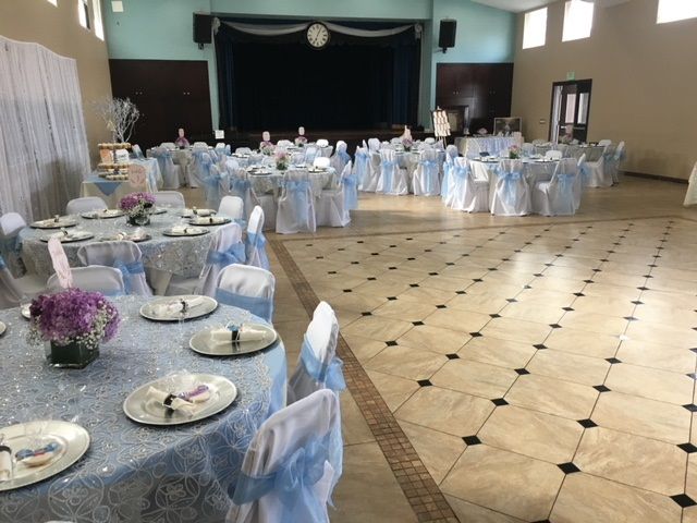 Elegant banquet hall with white-draped tables and chairs, set for a formal event with a stage at the back.