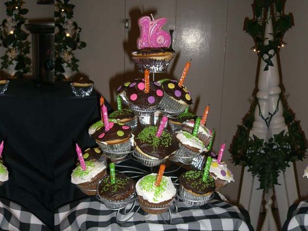 Pink “16” birthday cake centerpiece with cupcakes and lit candles on a decorated table