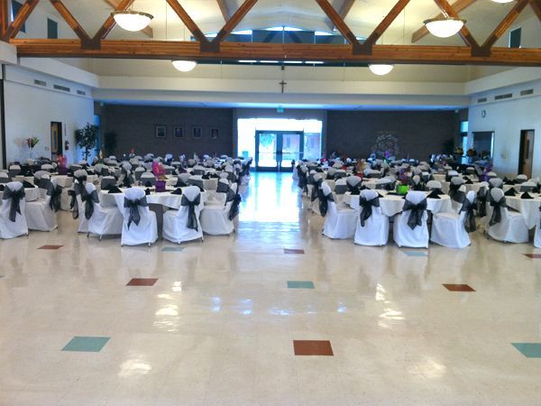 Banquet hall set for a formal event with round tables, white chair covers, and a stage at the far end