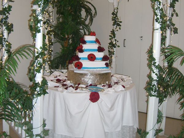 Tiered white cake with red and blue stripes and red roses on a decorated table with greenery