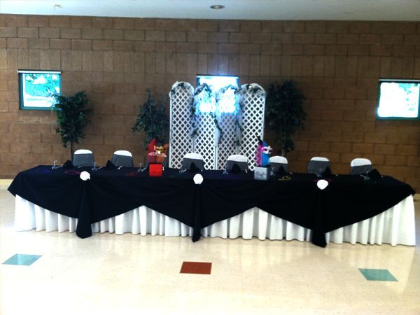 Decorated banquet table with black-and-white tablecloth in a lobby, flanked by plants and framed wall art.