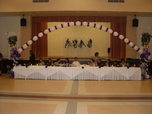 Banquet table on a stage decorated with purple-and-white balloon arch and floral arrangements