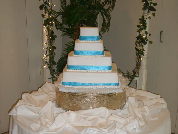 Tiered white cake with blue ribbons on a decorated table with white drapery and greenery backdrop