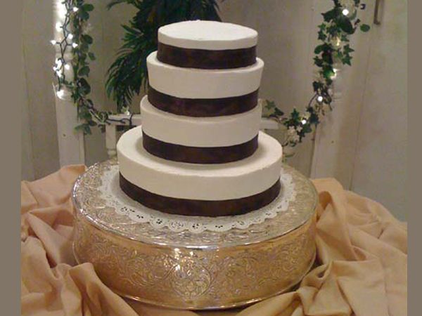 Tiered white and chocolate cake on a gold cake stand with draped beige fabric backdrop