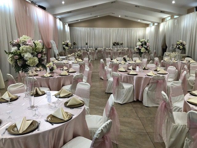 Elegant banquet hall with round tables, white chair covers, blush linens, and floral centerpieces ready for an event