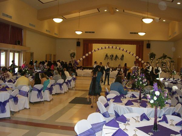 Banquet hall with decorated tables and guests seated facing a stage with an arch backdrop